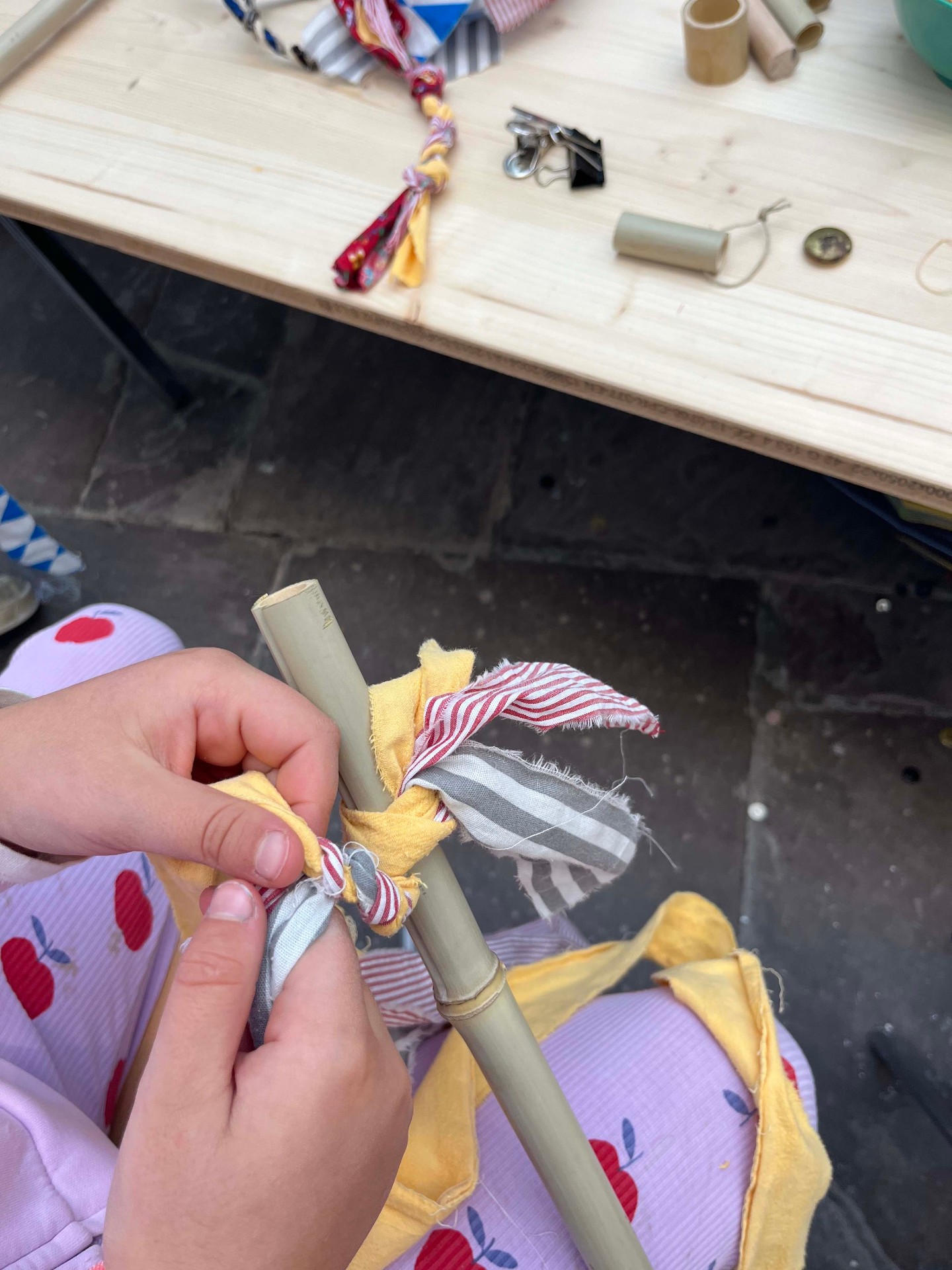 Child's hands tying striped and yellow fabric strips around a bamboo pole