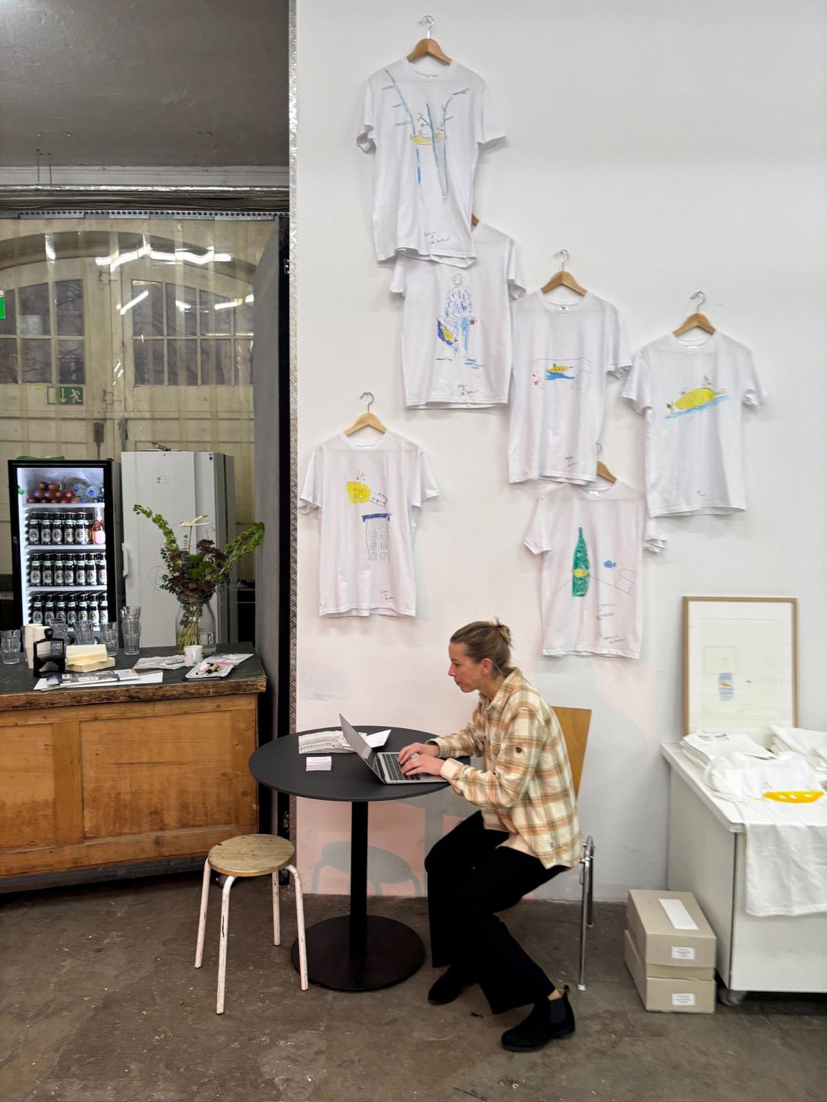 Illustrated T-shirts on wooden hangers in the exhibition space