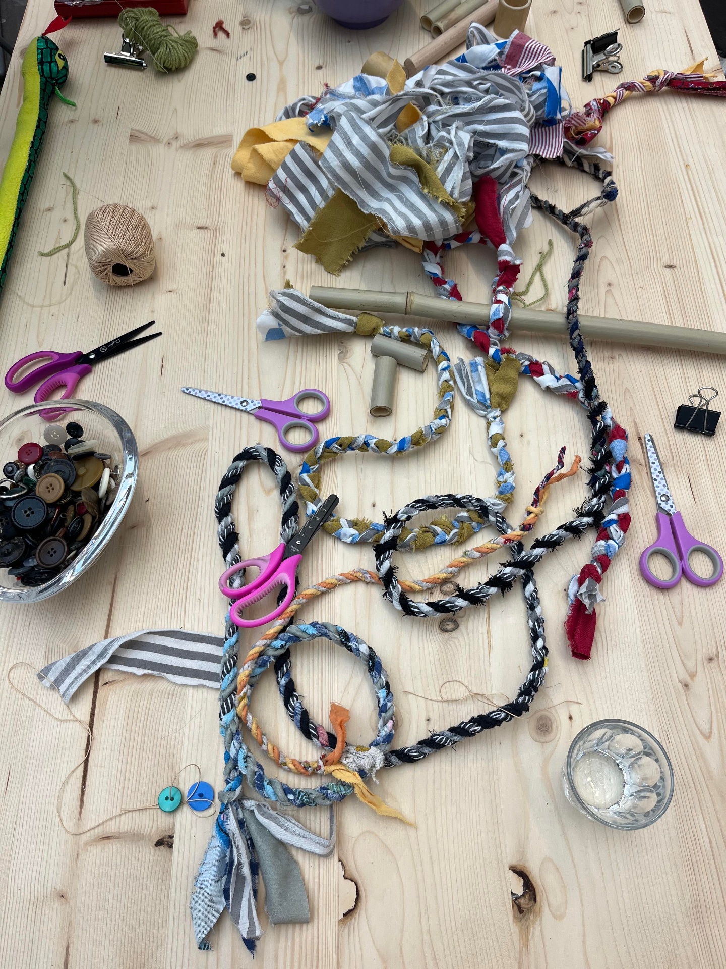 Workshop table with fabric scraps, braided fabric ribbons, scissors, buttons and bamboo tubes