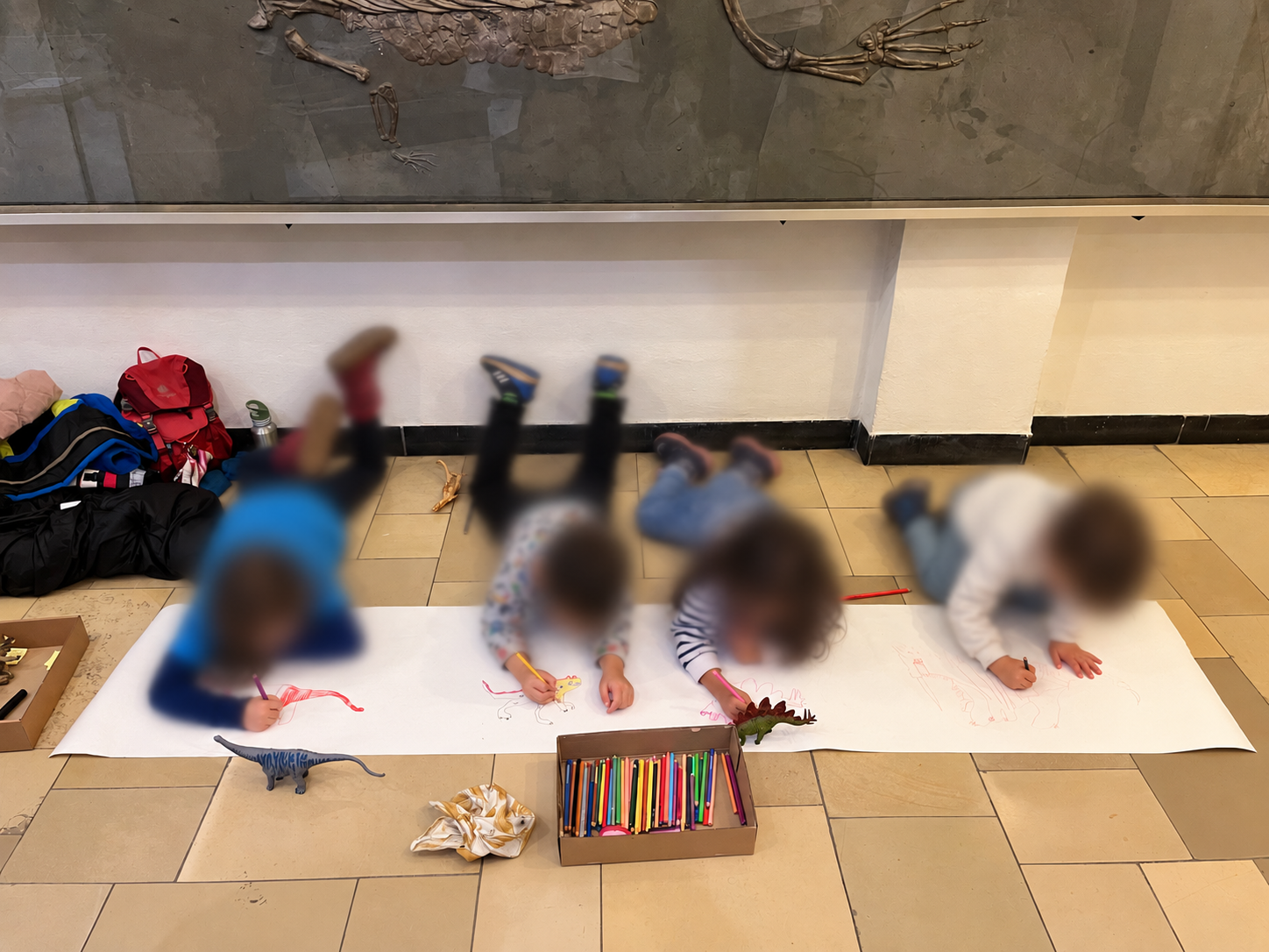 Children drawing together beneath a fossil display, with coloured pencils and dinosaur models