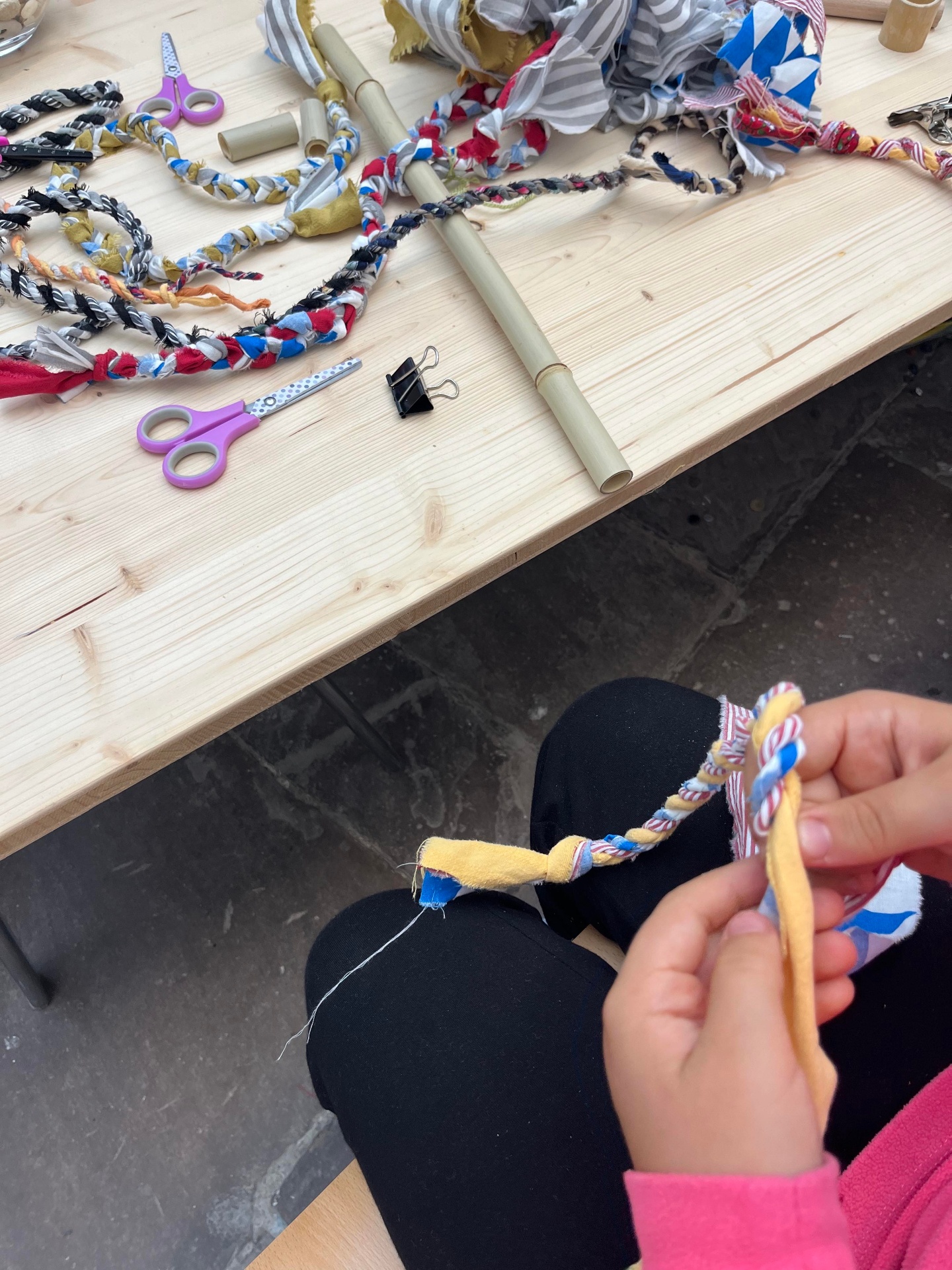 Hands braiding a colourful fabric cord made from leftover textiles