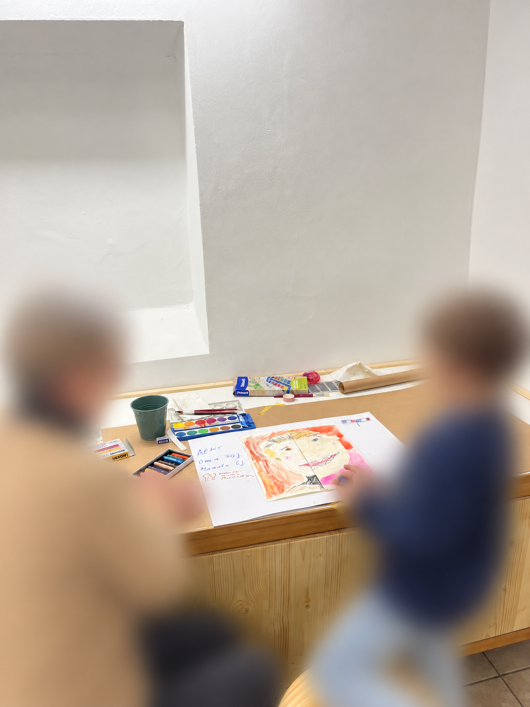 Grandparent and grandchild painting together at the studio table, faces blurred