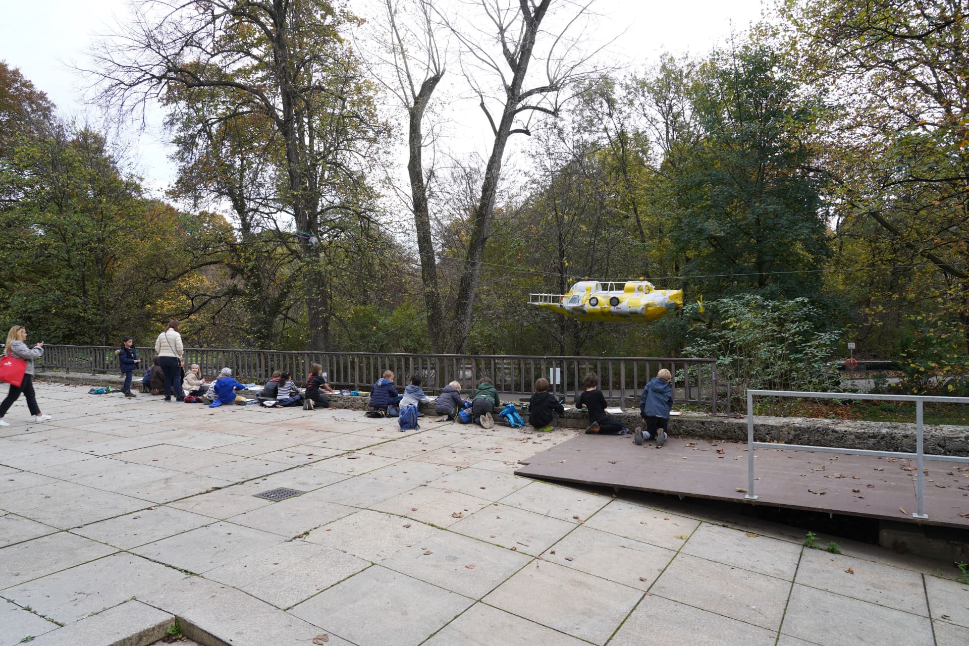 Children sketching the yellow submarine sculpture suspended among trees