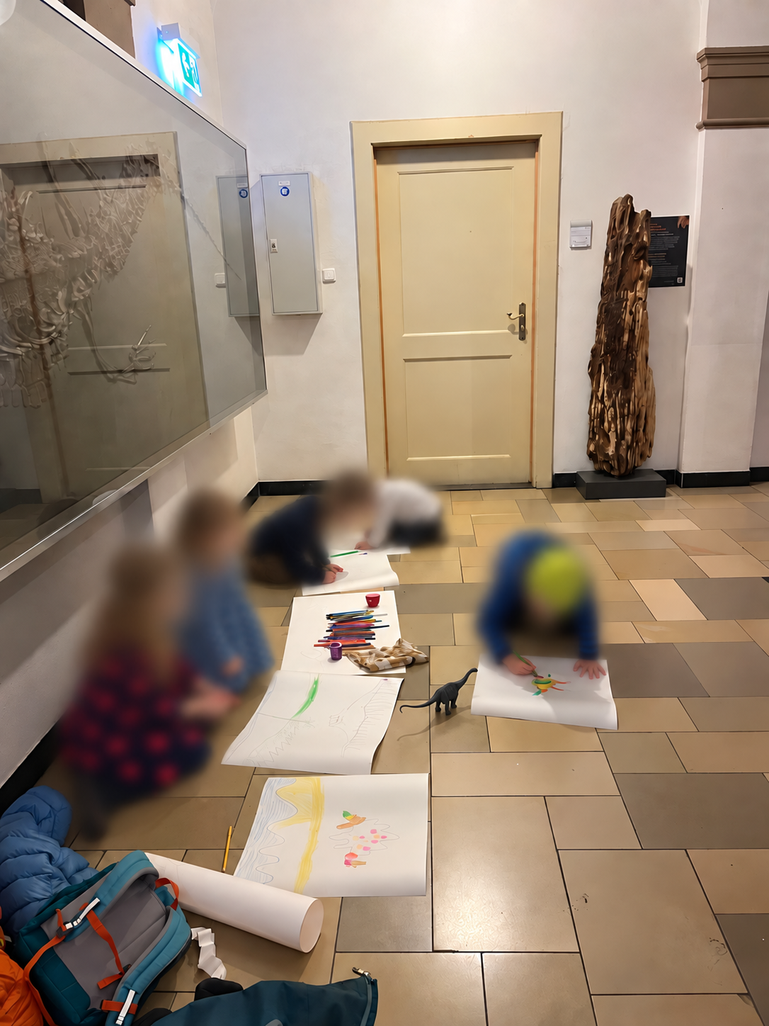 Children drawing dinosaurs on large sheets of paper in a museum