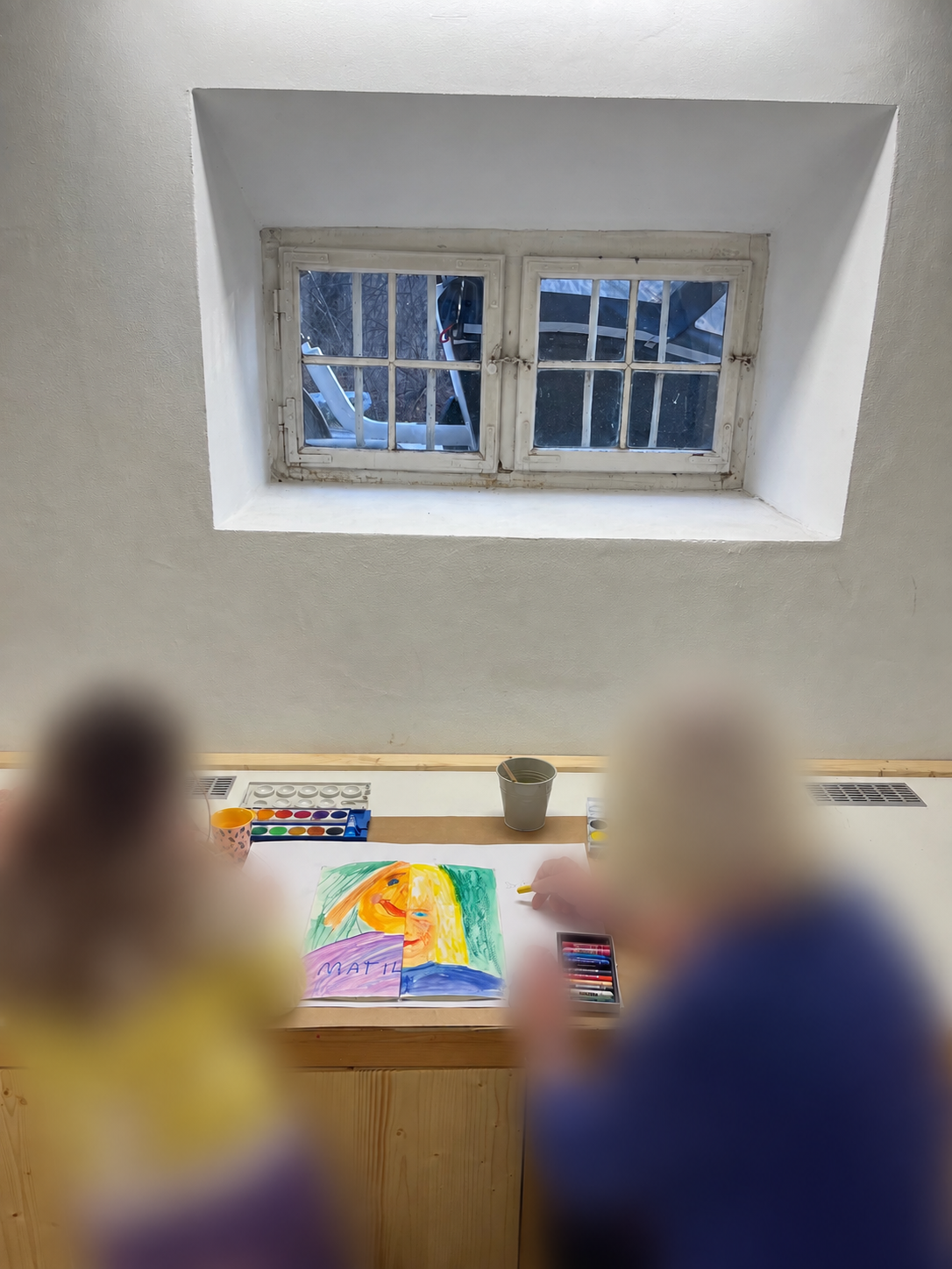 Two participants painting a shared portrait at the studio table, faces blurred